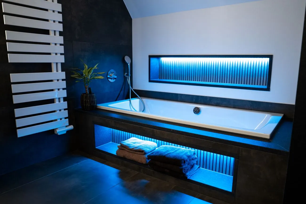 Badezimmer mit beleuchteter Badewanne und dunklem Design