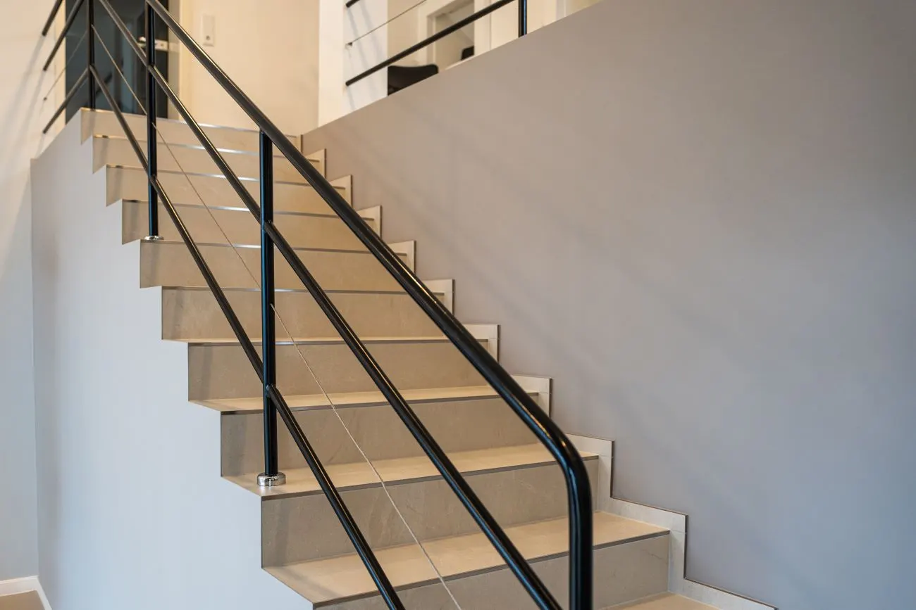 Moderne Treppe mit Fliesenstufen und schwarzem Geländer